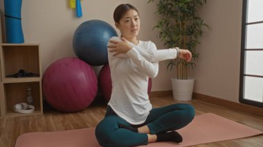 Spor salonunda yoga toplarıyla paspasın üzerinde uzanan, günlük spor kıyafetleri giyen, çekici ve odaklanmış, Çin 'de fitness ve rahatlama aktiviteleriyle meşgul bir kadın..