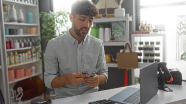 Delikanlı, dekoratif eşyalarla ve şık bir iç mekanda dizüstü bilgisayarla çevrili bir ev dekoratörü dükkanında para sayıyor.