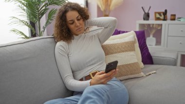 Rahat bir oturma odasında kanepede uzanan, modern dekor ve yastıklarla çevrili, rahat bir apartman dairesinde rahat bir öğleden sonra keyfine bakan bir kadın..