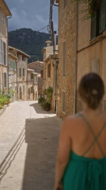Valldemossa 'da büyüleyici bir caddeyi keşfeden genç bir kadın, Mallorca manzaralı geleneksel taş evler bir dağ zeminine karşı