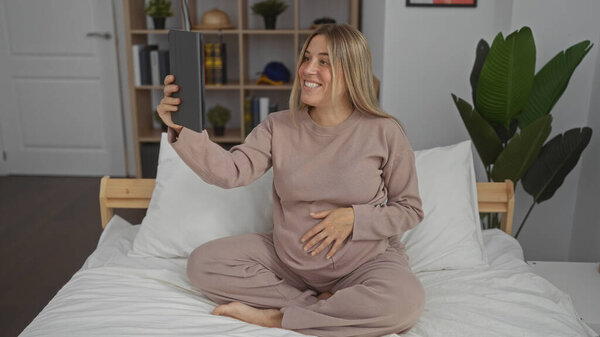 Беременная женщина делает селфи на кровати в уютной спальне, демонстрируя свой растущий живот и радостное ожидание в теплой домашней обстановке.