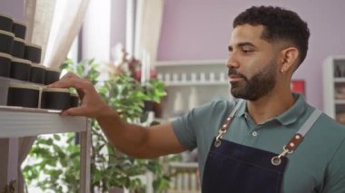 Bir ev dekorasyonu mağazasında genç bir adam çeşitli ev dekorasyonları ve yeşil bitkilerle raflardaki ürünleri inceliyor..