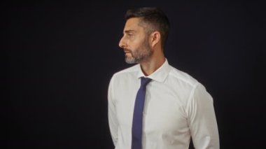 Beyaz gömlek ve kravat giyen çekici bir İspanyol 'un portresi, siyah bir arkaplanda izole edilmiş, kendinden emin ve profesyonel bir tavır sergiliyor..