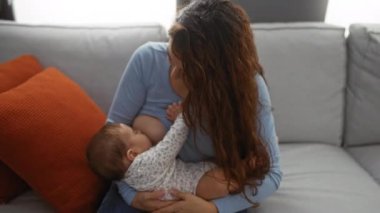 Anne, oturma odasındaki koltukta bebeği emziriyor. Evde bebek ve kadınla sevgi ve aile bağlarını gösteriyor. Evde dinleniyor.