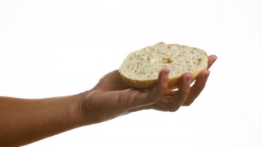 Dilimlenmiş bir simidi, izole edilmiş beyaz bir arka planda, basit bir duvarın üzerinde tutarak yemek sadeliğini ve kentsel atıştırmalıkları canlı bir şekilde resmediyor..