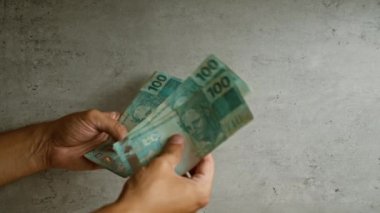 Elleri Brezilya 'nın parasını beton zemine karşı sayıyor. 100 banknotu canlı bir şekilde gösteriyor..