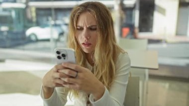 Gündüz vakti modern bir ofis ortamında evde oturmuş akıllı telefonlara bakan bir kadın..