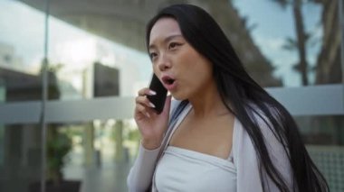 Şehir merkezinde telefonla konuşan, duygularını ifade eden, uzun saçlarını ve günlük kıyafetlerini sergileyen, arka planda modern mimarisi olan bir kadın..