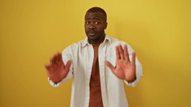 Afrika kökenli Amerikalı bir adam, eli kolu bağlı, tişört giymiş, izole edilmiş sarı arka planda güçlü duygularla hayal kırıklığını ifade ediyor.