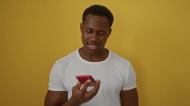 Akıllı telefonu parlak sarı arka plana karşı kullanırken gülümseyen genç adam modern iletişim ve teknolojiyi öneriyor.