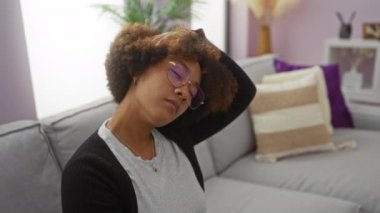 Rahat bir oturma odasında rahat bir kanepede otururken boynunu uzatan bir kadın doğal ışık ve asgari dekor ile ev içinde sakin bir atmosfer yaratıyor..