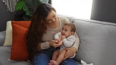 Anne ve bebek oturma odasındaki rahat bir kanepeye oturur, sıcak tonlarda ve nazik ifadelerle aile sevgisini ve içeride kaynaşmayı gösterir..