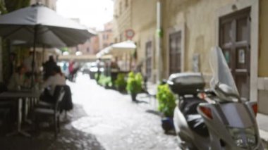 Roma 'da insanların şemsiyeler altında yemek yediği ve kaldırım taşı bir sokakta park etmiş bir scooter' ın eski bir İtalyan kasabasının ruhunu yakaladığı bulanık bir manzara..