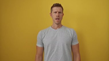 Genç adam canlı sarı bir arka plana karşı duruyor, etkileyici bir görünüşü var, günlük gri bir gömlek giyiyor, kendinden emin ve çekici bir tavır sergiliyor..