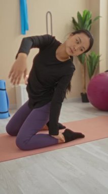 Genç Çinli kadın yoga yaparken spor salonunda siyah bluz ve mor tayt giyerek poz veriyor.