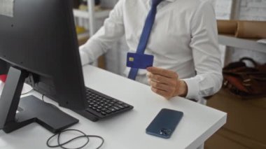Modern ofiste bilgisayar kullanan bir işadamı, elinde online alışveriş veya mali işleri gösteren odaklı ifade gösteren bir kredi kartı tutarken,
