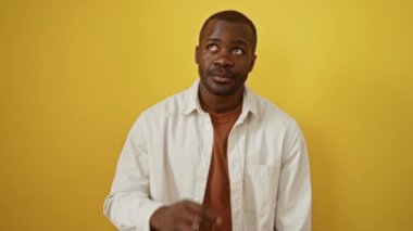 Üzerinde bir fikir olan tişört giyen Afrikalı Amerikalı bir adam bir numarayı işaret ediyor, mutlu ve başarılı bir şekilde izole edilmiş sarı arka planda.