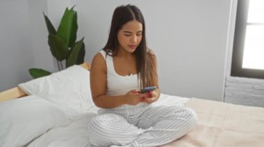 Yatak odasında rahat bir şekilde selfie çeken bir kadın. Akıllı telefonlu pijamalar giyiyor. Modern ev ortamında rahat ve mutlu bir ruh hali sergiliyor..