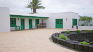 Lanzarote 'de yeşil kapıları olan ve bulutlu gökyüzü altında siyah volkanik kayalar ve yeşillik barındıran bulanık bir koloni tarzı bina.