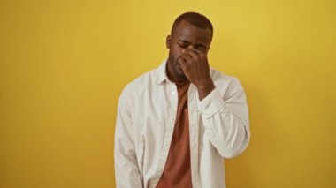 Dostum, Afro-Amerikan tişörtü giyen, izole edilmiş sarı arka planda duran, yorgun gözler sürtünen, stresten dolayı baş ağrısı, yorgunluk, hayal kırıklığı ve baş ağrısı