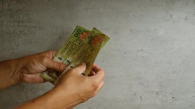 Adam, somut bir zemine karşı Arjantin pesolarını sayarak parmak uçlarını ve para biriminin detaylarını ince bir dokuyla vurguluyor..