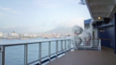 Mavi gökyüzünün altındaki korkuluk ve uzak şehir manzarasıyla bir gemi güvertesinin bulanık görüntüsü seyahat ve deniz atmosferinin özünü yakalıyor..