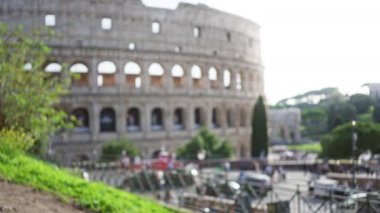 Roma, İtalya 'daki ikonik kolezyumu ön planda bulanık yeşillik ve tarihi mimariyi vurgulayan bir bokeh etkisi ile görüntüden çıkarılmış görüntü.