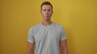 Genç bir adam parlak sarı bir arkaplan önünde komik bir yüz yapıyor, neşeli yüz ifadesini ve parlak, izole bir ortamda günlük gri gömleğini vurguluyor..