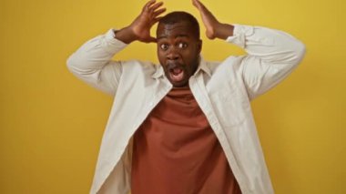 Afrika kökenli Amerikalı bir adam, elleri şokta, sarı arka planda, şaşkın bir ifadeyle, gömleğini giyer ve ağzını kocaman açar, korkmuş görünür, çılgın bir poz verir.