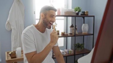 İspanyol bir adam spa odasında tarakla şarkı söylüyor, arkasında hafif ışıklandırma ve güzellik ürünleriyle içeride eğlence ve rahatlama gösterisi yapıyor..