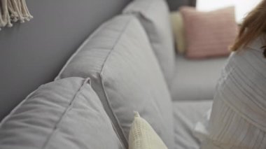 Oturma odasında yastıkları olan, kulaklık takan ve müzik dinleyen, kendini huzurlu bir apartman dairesine daldıran bir kadın.