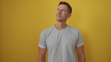 Gri gömlekli genç adam, parlak sarı arka plana karşı duruyor. Düşünceli bir ifade ve minimalist bir portrede sıradan bir duruş..