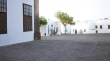 Lanzarote, İspanya 'da beyaz binalar, yeşil ağaçlar ve kaldırım taşı yolu olan beyaz bir açık hava caddesinin odaksız görüntüsü..