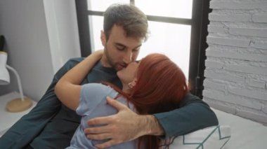 Sıcak bir evde yatakta kucaklaşan bir çift şık bir yatak odasında sevgi ve yakınlık sergiliyor. Bir erkek ve bir kadın, sakin bir ortamda hassas bir anı paylaşıyor..