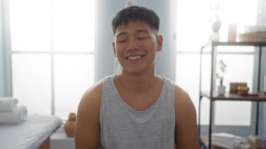 Sağlık merkezindeki yakışıklı, gülümseyen ve spa odasında dinlenen gri kolsuz tişörtlü genç adam.