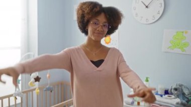 Afro-Amerikalı kadın, mutlu bir yüzle ayakta duran, bebek odasında elleri olan bir süveter giyiyor. Parmakları, hayal gücünü ve kompozisyonu vurgulayan yaratıcı bir fotoğraf konsepti.