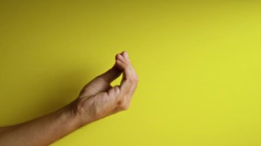 İnsan eli, canlı sarı bir arkaplan önünde İtalyan jesti yapıyor. Kültürel ifade ve görünür parmaklar ve bileklerle iletişimi vurguluyor..