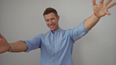 Beyaz arka planda sevinçle gülümseyen bir adam mavi gömlekli ve kolları açık bir şekilde portre tarzı bir resimde mutluluğu izole edilmiş minimalist bir ortamda gösteriyor..