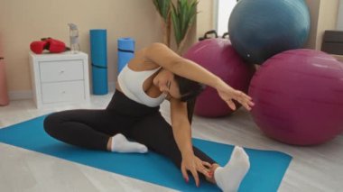 Spor salonunda spor toplarıyla paspasa uzanan kadın, spor merkezi iç dekoruna odaklanmış ve rahatlamış görünüyor..