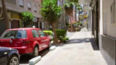 Açık havada güneşli bir günde park halindeki kırmızı araba ve palmiye ağaçları ile bulanık sokak manzarası