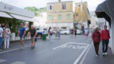 Capri Adası 'ndaki bulanık sokak sahnesinde yürüyen insanlar tarihi binalar ve canlı bir ambiyansla.