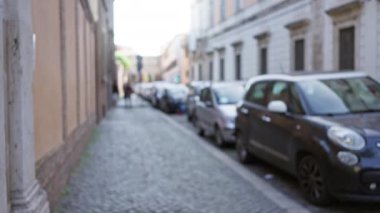 Roma 'da park halindeki arabaların ve kaldırım taşı bir yolda geleneksel mimarinin bulunduğu bulanık bir sokak manzarası İtalyan kentsel ortamının özünü yakalıyor..