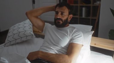 Beyaz gömlek giyen sakallı yakışıklı bir adam yumuşak ışıklandırmalı, iç gözlem ya da tefekküre dayalı, rahat bir yatak odasında yatıyor.