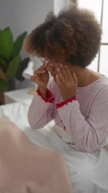 Yatak odasında kıvırcık saçlı bir kadın. Parlak iç odada tapınakları tutarken dalgın dalgın bakıyor.