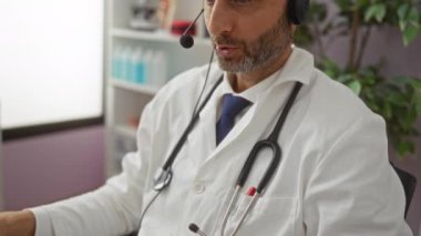 Hastane ofisinde teletıp konseptini stetoskop ve tıbbi ekipmanla birlikte profesyonel bir sağlık ortamında gösteren bir bilgisayar aracılığıyla iletişim kuran bir doktor..