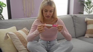 Oturma odasında rahat bir koltukta oturan bir kadın, endişeli bir ifadeyle hamilelik testi tutuyor, bir ev ortamında beklenti ve duygu anı yakalıyor..