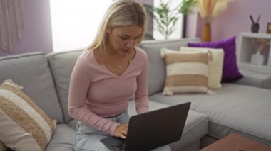 Rahat bir oturma odasında dizüstü bilgisayarla rahatlayan, günlük kıyafetler giyen, teknolojiyi kucaklayan ve rahat bir koltukta huzurlu bir anın tadını çıkaran bir kadın..