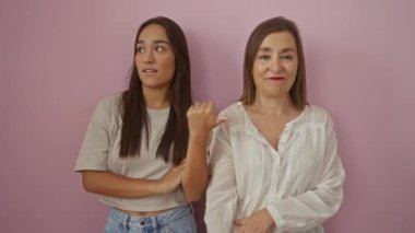 Anne ve kızı pembe duvara karşı durarak sevgi dolu jestler ve şakacı ifadeler sergiliyorlar, gündelik giysiler giyiyorlar, sevgi dolu bir aile ortamında birbirlerine bağlanıyorlar.