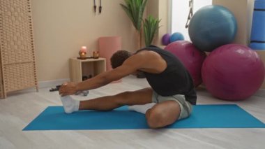 Spor salonunda yoga minderinde uzanan genç bir adam. Egzersiz topları, bitkiler ve mumlar, sakin bir iç mekan çalışma ortamını gösteriyor.