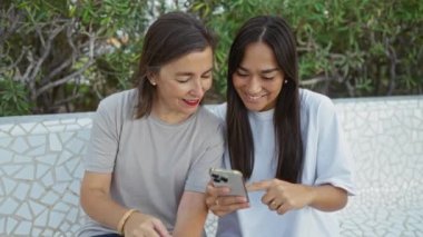 Parkta birlikte vakit geçiren kadın ve kız akıllı bir telefona bakarken, anı paylaşırken, gülümserken, sıcak, aile, kentsel ve dostane bir atmosfer yaratırken..